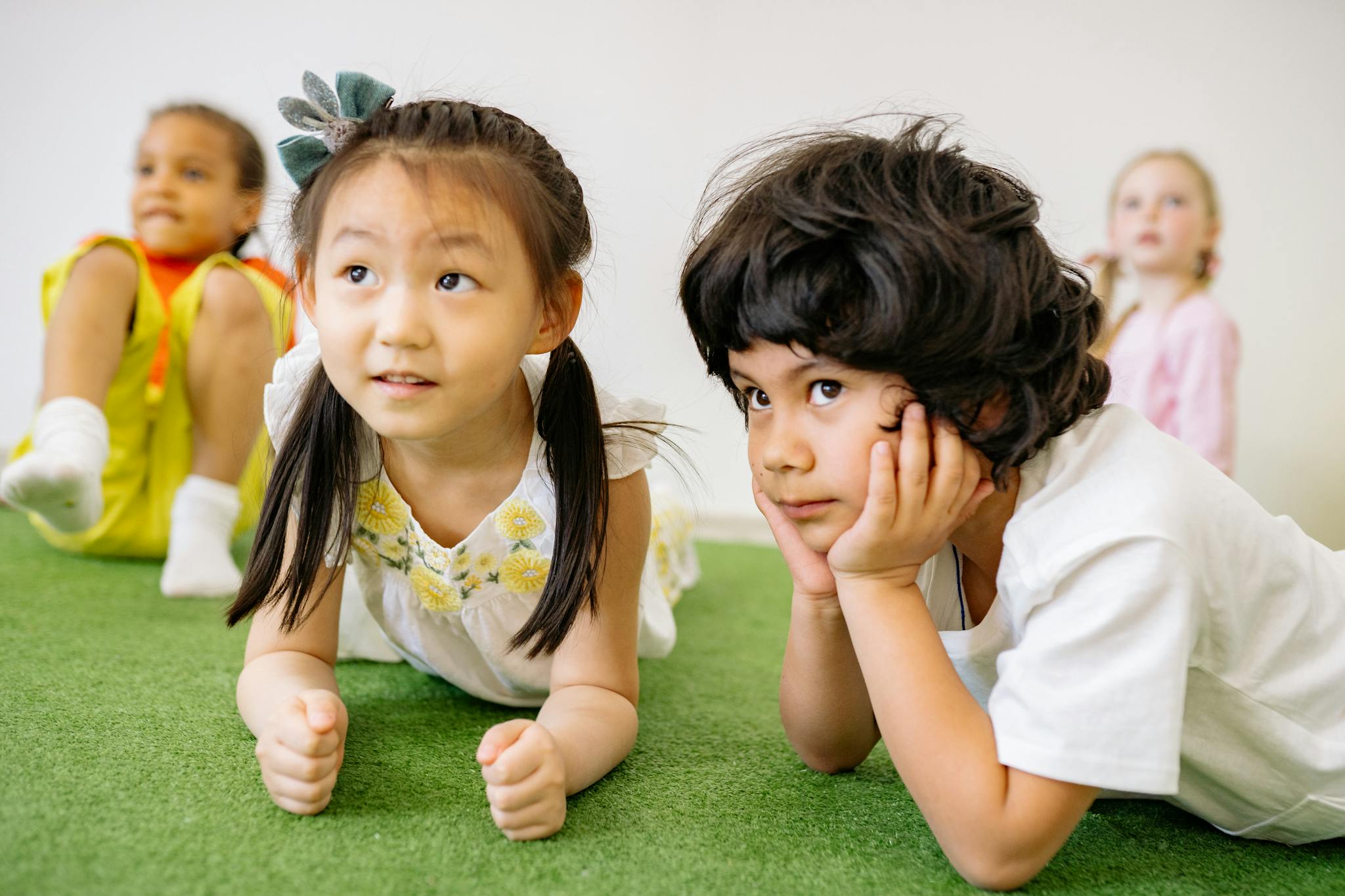 Group of children lying on grass indoors, enjoying a playful learning activity in kindergarten.